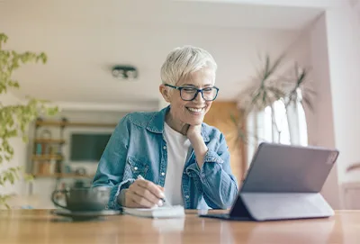 Older woman on virtual call taking notes