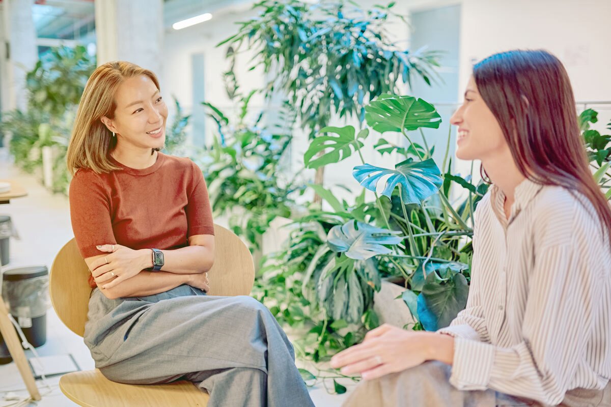 two women sitting talking in front of plants