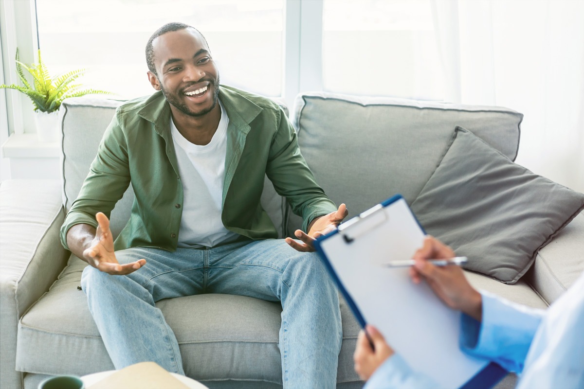 man sitting on couch talking to person with clipboard
